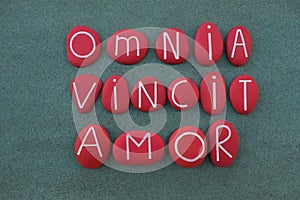 Omnia Vincit Amor, Love conquers all, latin phrase, Virgil poet, text composed with red colored stone letters over green sand photo