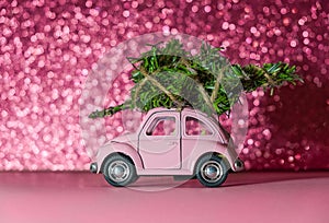 Omsk, Russia - Oktober 27, 2018: toy model car with Christmas tree on on the roof rides on pink Blurred Glitter background.