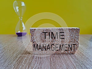 ?oncept for time management. Brick blocks and hourglass on beautiful yellow background.