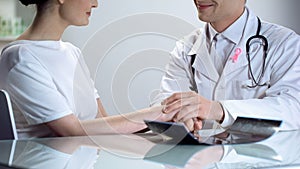 Oncologist telling young lady good news, no threat of breast cancer both smiling