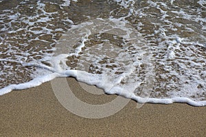 Oncoming Sea waves with foam on to a Sandy beach.