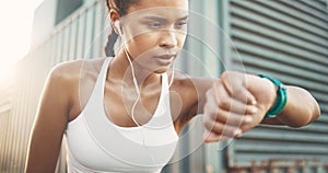 One active young hispanic woman wearing earphones and checking digital smartwatch while exercising in an urban setting