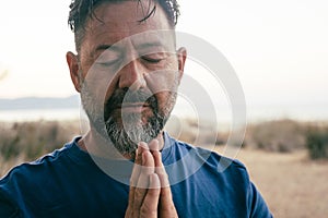 One adult man praying and meditate outdoor in relaxation gesture with hands clasped and closed eyes portrait. Zen like healthy