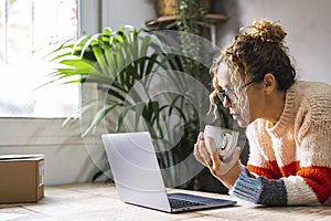 One adult woman watching laptop screen and drinking hot beverage coffee at the table. Home worker online business. Lady surfing