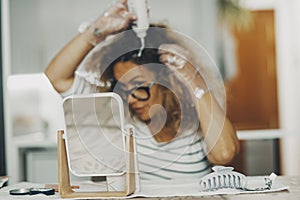 One alone woman in background putting cream treatment on her brown hair. Mirror on focus in foreground. Concept of single