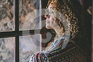 One alone woman standing at home near the window looking outside and thinking. Single female people lifestyle. Waiting friends and