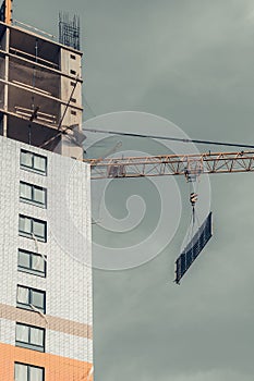 One amber high-rise crane hauling plate against a house and gray sky during the construction phase. Industry concept