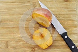 One Amigo Pluot Cut Open with a Knife on a Wood Chopping Board