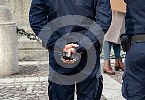 One anonymous policeman in a blue uniform holding a walkie talkie radio, hands closeup, arms behind back. Communication, police