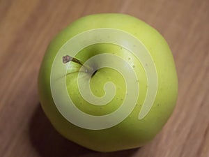 One apple of Golden cultivar on a wooden surface. Close-up shot