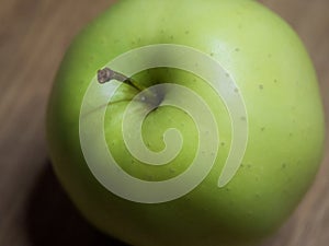 One apple of Golden cultivar on a wooden surface. Close-up shot