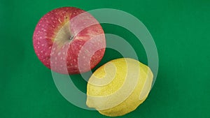 One apple and one lemon isolated on green table