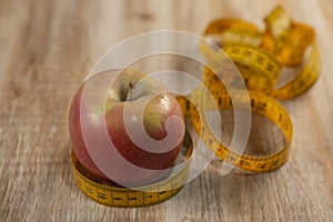 One apple surrounded by a tape measure and on weathered wood background