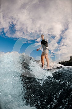 one-armed man ride the wave on wakeboard against the background of cloudy sky.