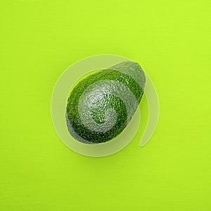 One avocado on green background, top view.