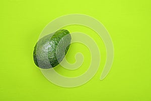 One avocado on green background, top view.