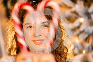 One beautiful curly-haired girl stands near the tree, New Year photo session with candy lollipop