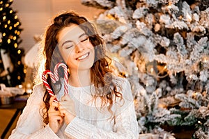 One beautiful curly-haired girl stands near the tree, New Year photo session with candy lollipop