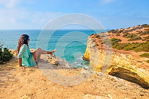 One beautiful sexy girl sits on stones on a rock in Portugal. back view of the ocean