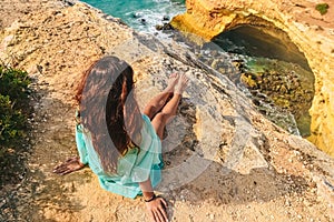 One beautiful sexy girl sits on stones on a rock in Portugal. back view of the ocean