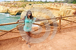 One beautiful sexy girl stands with a large backpack near a fence on a rock in Portugal and looks straight. ocean view