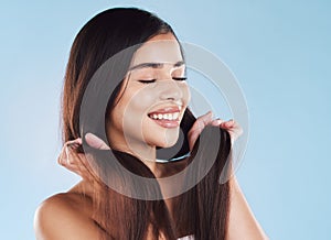 One beautiful young hispanic woman touching her sleek, silky and healthy long hair while smiling against a blue studio