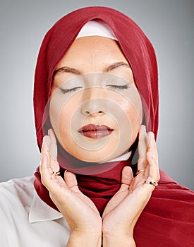 One beautiful young muslim woman with eyes closed wearing red headscarf and lipstick against grey studio background