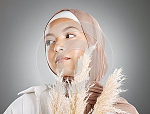One beautiful young muslim woman wearing brown headscarf holding a pampas wheat plant isolated against grey studio