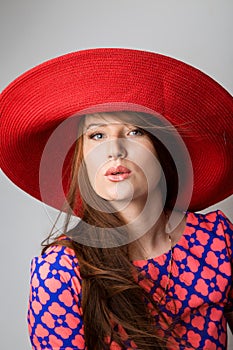 One beautiful young woman blowing a kiss in red blue dress and a hat isolated white grey background . Studio shot, vertical image