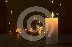 One big candle and flame of it on the wooden surface against glass background and lights