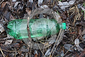 One big green plastic bottle lying on brown earth and leaves