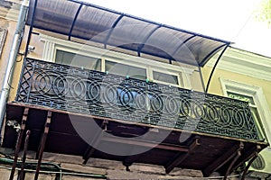 One big open old balcony with black iron bars with a forged pattern on the brown concrete wall