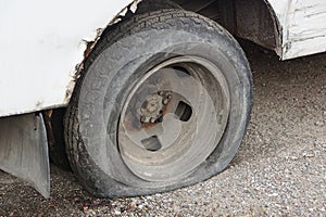 One black flat tire on a white car on gray asphalt