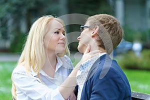 One blond european woman holding neck of her lover and waiting his kissing in some park at warm summer day