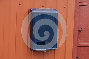 One blue iron mail box hanging on a red metal fence