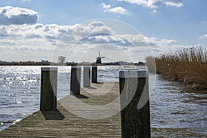 One of the boat docks with mooring posts in the lake de Rottemeren with the windmill Tweemanspolder nr 4 in the background on a su