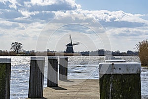 One of the boat docks with mooring posts in the lake de Rottemeren with the windmill Tweemanspolder nr 4 in the background on a su