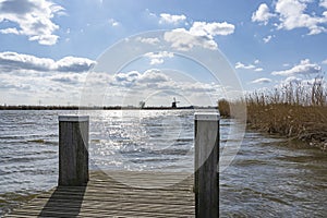 One of the boat docks with mooring posts in the lake de Rottemeren with the windmill Tweemanspolder nr 4 in the background on a su