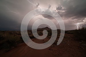 One bolt of lightning strikes in the distance while another zigzags across the sky lighting the desert below Gooseberry Mesa