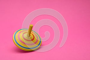 One bright spinning top on pink background, space for text. Toy whirligig