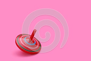 One bright spinning top on pink background, space for text. Toy whirligig