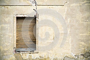 One brown grungy yellow wooden window in a gray yellow broken cracked facade of an abandoned derelict house