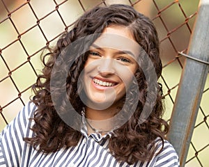 One brunette teenager smiling by rusty fence