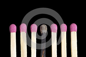 One burnt match among six new matches in a row isolated on black background