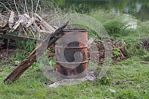 One burnt old iron red black barrel with a wooden gray board stands in green grass