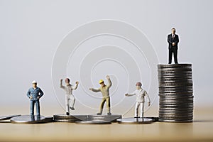 One businessman standing on highest coins stacking and many workers standing on lower coin for different income and unequal in