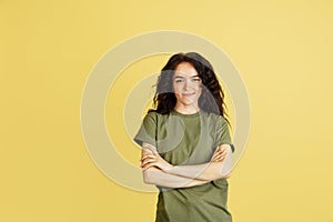 One calm, smiling Caucasian woman with arms folded on chest posing isolated over yellow studio background.