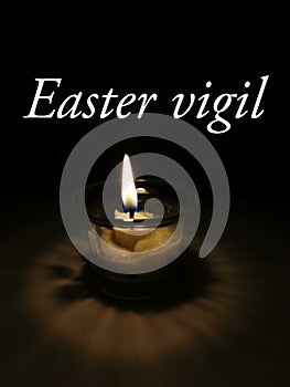 One candle burn brightly on dark background with word written Easter Vigil.