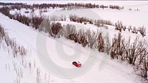 One car is driving along a winter snowy country road. Aerial view from the drone.