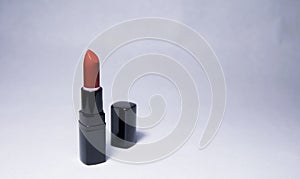 Carrot-colored lipstick stands vertically open with a black cap near in the center on a white background photo